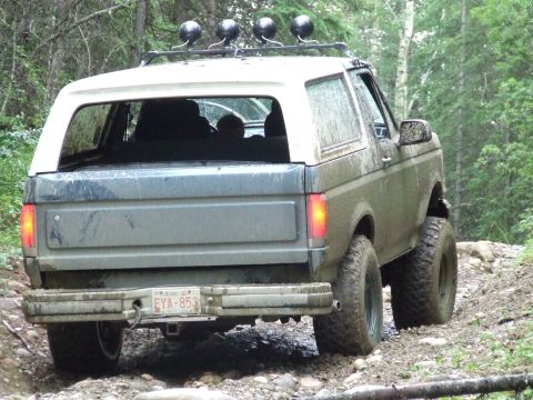 1990 Ford Bronco - A muddy 1987 Ford Bronco navigates a rocky, wooded trail from a rear perspective.