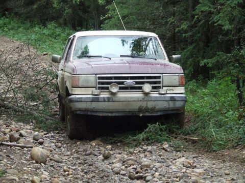 1990 Ford Bronco - 1990 Ford Bronco navigating a rough, rocky path through a forest.
