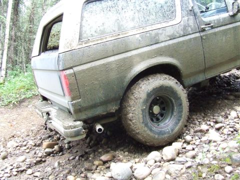1990 Ford Bronco - Mud-splattered 1990 Ford Bronco navigates a rocky, off-road trail.