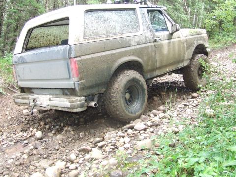 1990 Ford Bronco - 1990 Ford Bronco navigating a rough, rocky path in a wooded area.