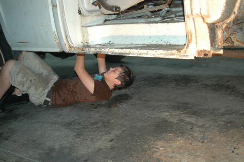 1963 Ford F-250 - A person works on the underside of a white 1963 Ford F-250 truck.