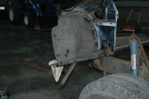 1963 Ford F-250 - This image shows the inner fender well and part of the frame of a disassembled truck, with a tractor in the background.