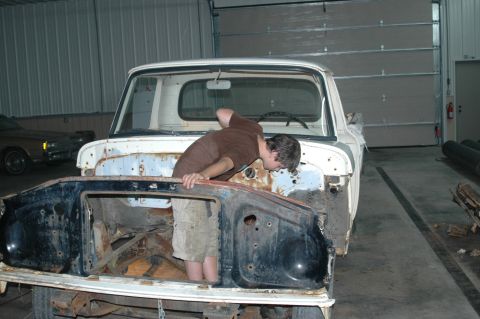 1963 Ford F-250 - Person working inside the engine bay of a disassembled 1963 Ford F-250 truck.