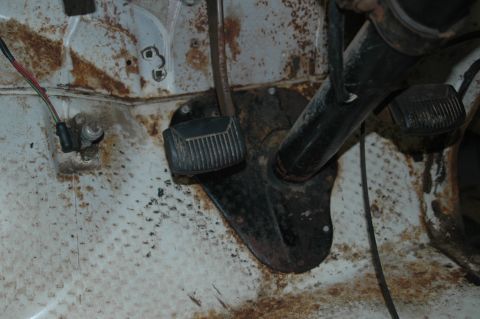 1963 Ford F-250 - The interior floor of a vehicle shows significant rust around the pedals and wiring harness.