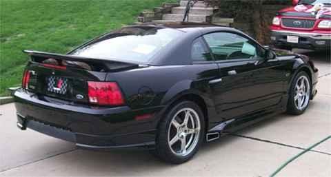2001 Ford Mustang - A black 2001 Ford Mustang coupe is parked on a driveway, with a red truck in the background.