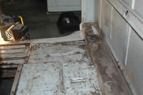 1963 Ford F-250 - The interior floor of a truck shows signs of wear and rust, with a portable work light visible in the background.