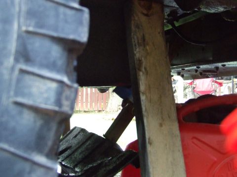 1990 Ford Bronco - The vehicle is supported by wood and surrounded by repair equipment, with a fence visible in the background.