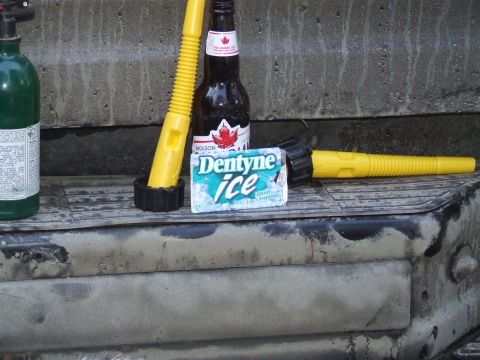 1990 Ford Bronco - A collection of items including a gas can, beer, gum, and fuel spouts are arranged on a weathered surface.