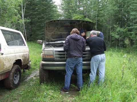 1990 Ford Bronco - Two men work on the engine of a 1990 Ford Bronco, with another Bronco nearby.