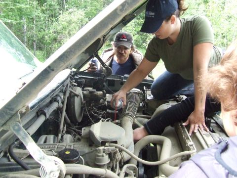 1990 Ford Bronco - People working on a vehicle's engine bay, with one person spraying something into the air intake.