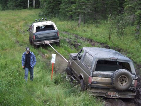 1990 Ford Bronco - Two Ford Broncos navigate a muddy trail, with one vehicle assisting the other.
