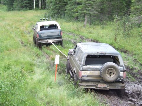 1990 Ford Bronco - Two Ford Broncos navigating a muddy trail, one pulling the other out.