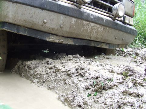 1990 Ford Bronco - Vehicle stuck in mud, showing front bumper and tire submerged.