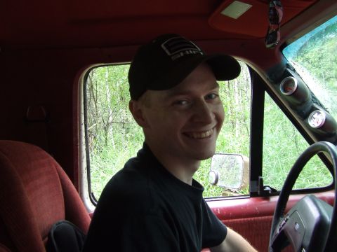 1990 Ford Bronco - Man smiles from the interior of a vehicle, with trees visible through the window.