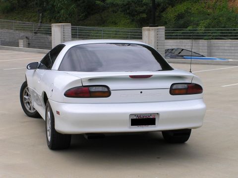 2001 Chevrolet Camaro - Rear view of a white 2001 Chevrolet Camaro parked in a lot, with trees and a fence in the background.