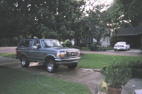 1995 Ford Bronco - A gray Ford Bronco is parked in a driveway next to a house, with a white sedan visible in the background.