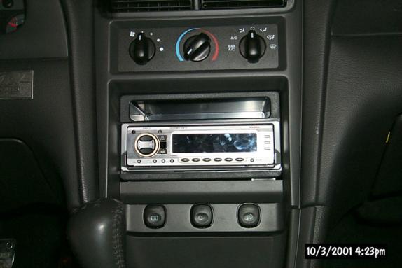 Aftermarket car stereo head unit below three-knob climate controls in a dark dashboard