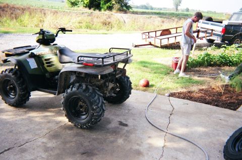 1995 Ford Bronco - A green ATV is parked on a concrete surface with a trailer and truck in the background.
