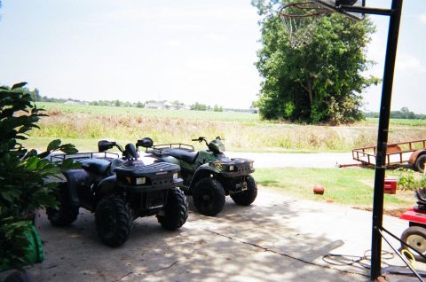 1995 Ford Bronco - Two all-terrain vehicles are parked outside on a sunny day, with a field and trees visible in the distance.