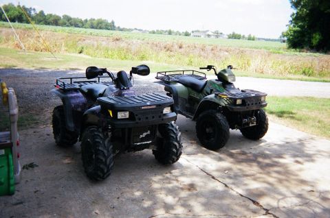 1995 Ford Bronco - Two ATVs are parked on a concrete driveway in front of a field.