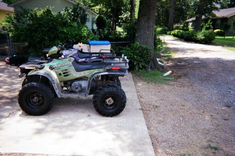 1995 Ford Bronco - A green Polaris Sportsman 4x4 ATV is parked on a concrete pad next to a gravel driveway.