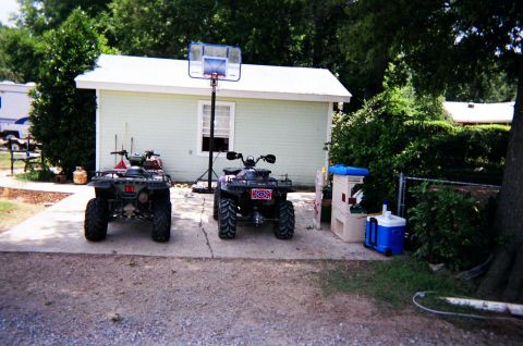 1995 Ford Bronco - Two ATVs are parked on a concrete driveway next to a building and a fence.