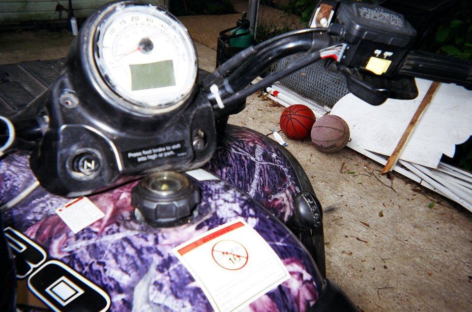 ATV dashboard with gauge, handlebars, and fuel cap; two basketballs are nearby