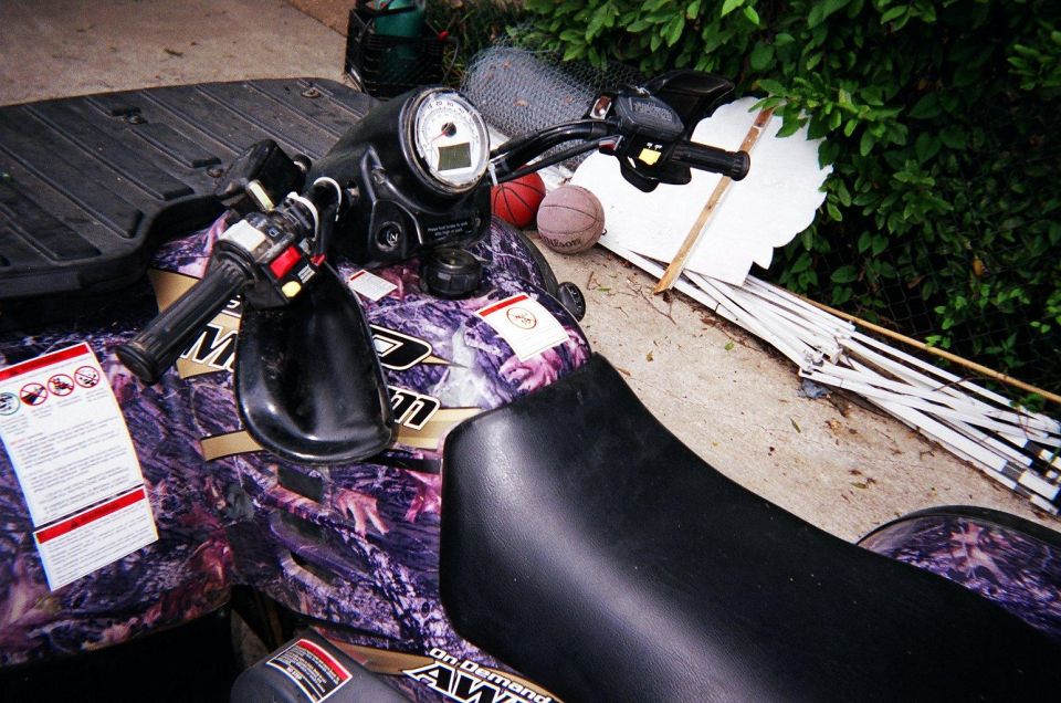 ATV handlebars, seat, and camouflage body. Two basketballs are behind the handlebars