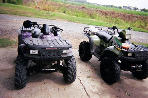 1995 Ford Bronco - Two all-terrain vehicles are parked side-by-side on a concrete surface, with a rural landscape visible behind them.