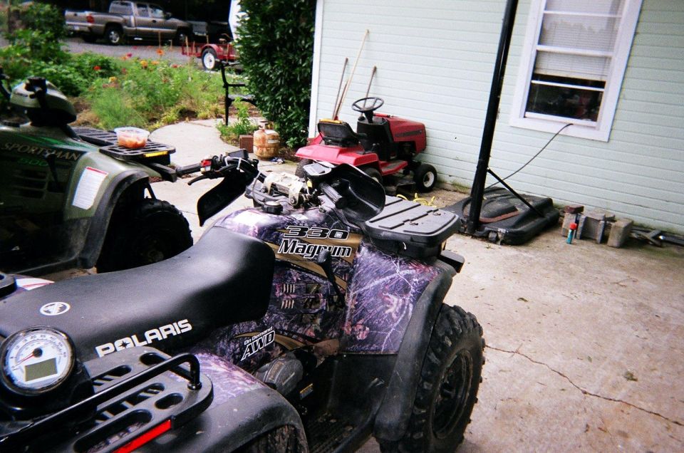 Two ATVs and a red lawnmower parked on a concrete driveway next to a house
