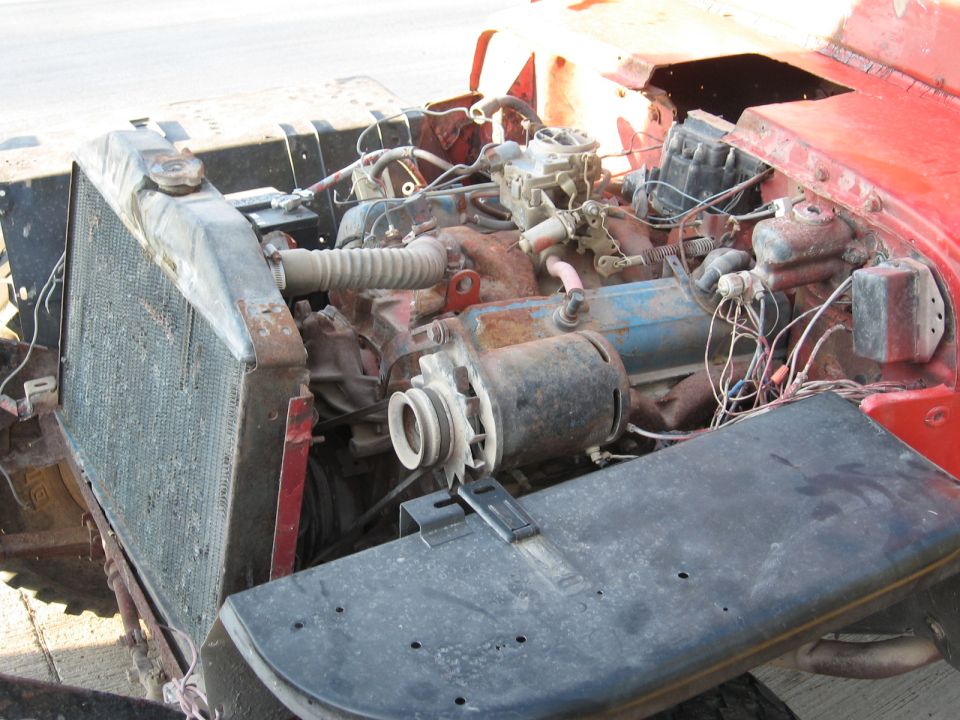 Exposed, rusty engine bay of a red pickup with radiator detached and hood removed