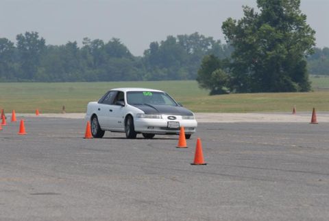 1992 Ford Taurus - White 1992 Ford Taurus navigates a course marked by orange cones, a contrasting black hood and race number 59.