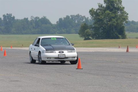1992 Ford Taurus - White 1992 Ford Taurus with a black hood navigates a course marked by orange cones.