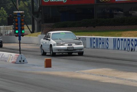 1992 Ford Taurus - White 1992 Ford Taurus with black hood on drag strip, Memphis Motorsports sign in background.