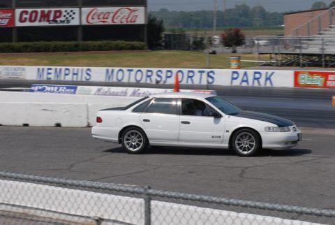 1992 Ford Taurus - A white sedan with a black hood is on the track at Memphis Motorsports Park, with grandstands visible.