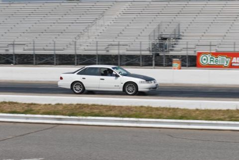 1992 Ford Taurus - A white sedan with a black hood is seen on a race track with grandstands in the background.