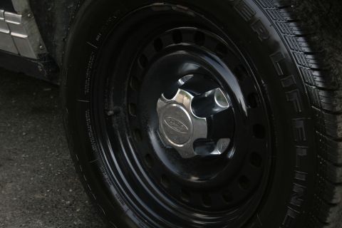 1989 Ford Crown Victoria LTD - Close-up of a black steel wheel with a Ford hubcap and tire, showing part of the vehicle's side panel.