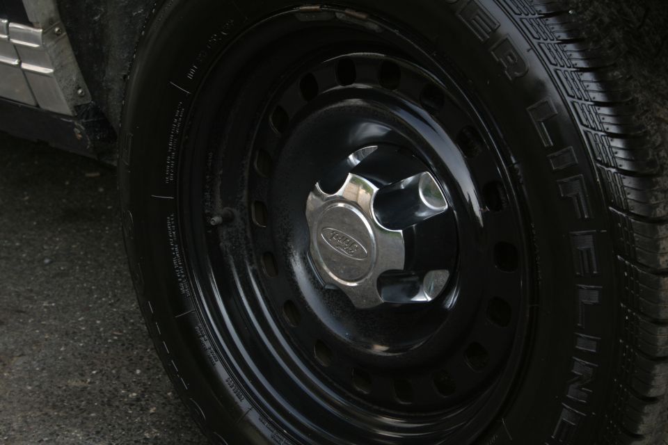 Black steel wheel with a chrome Ford hubcap and a black tire. The side panel of the vehicle is visible