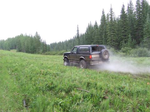 1988 Ford Bronco - A black Ford Bronco drives off-road, creating a dust cloud on a cloudy day.