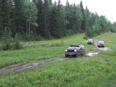 1988 Ford Bronco - Several SUVs navigate a muddy track through a wooded area.