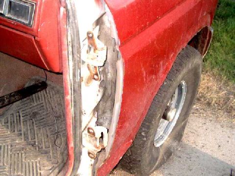 1986 Ford Bronco - The interior of a red SUV is visible, with a focus on the door hinges and a worn floor mat.