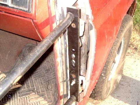 1986 Ford Bronco - Close-up view of a red vehicle's door frame, showing a custom tube door mounting bracket and a portion of the tire.