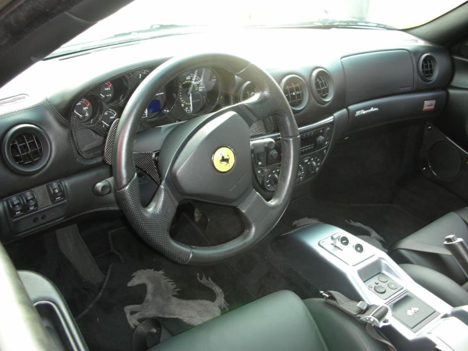 Black leather interior of a Ferrari 360 showing wheel with horse badge and gated shifter