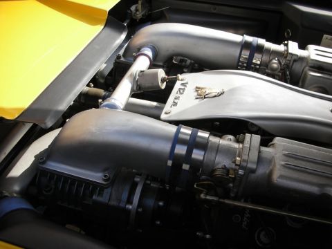 1998 Ford Crown Victoria - engine bay of a yellow V12 sports car reveals polished intake plenums, blue clamps and twin air boxes.