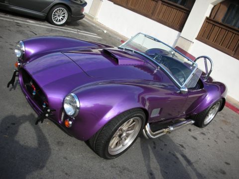 1998 Ford Crown Victoria - purple metallic Cobra-style open roadster with chrome side exhaust and polished wheels parked at an angle on a street.