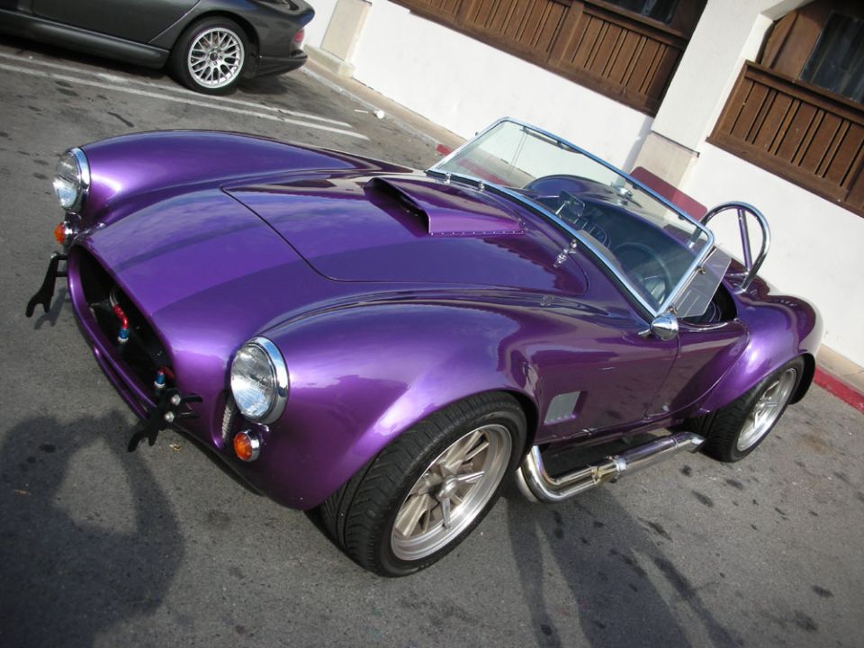 Purple metallic Shelby Cobra-style roadster parked on pavement, front three-quarter view