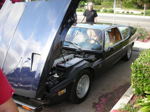 1998 Ford Crown Victoria - dark blue Lamborghini Espada-style four-seat coupe with its front hood raised and a man standing beside it.