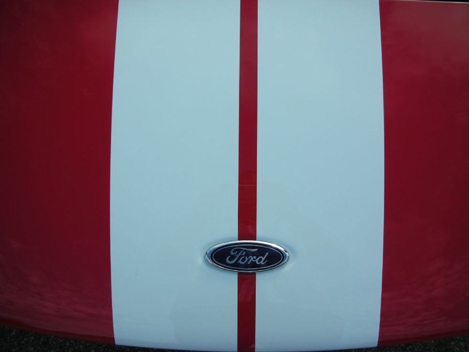 Red car hood with white center stripe and chrome Ford oval emblem
