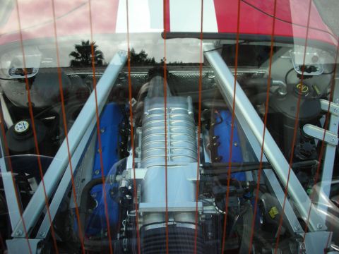 1998 Ford Crown Victoria - mid-mounted engine topped by a polished supercharger and blue covers, seen through red rear-window slats.