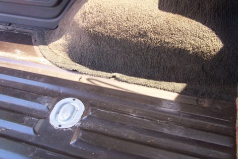 1990 Ford Bronco - Close-up of a cargo tie-down anchor in the interior of a vehicle, with carpeted trim visible.